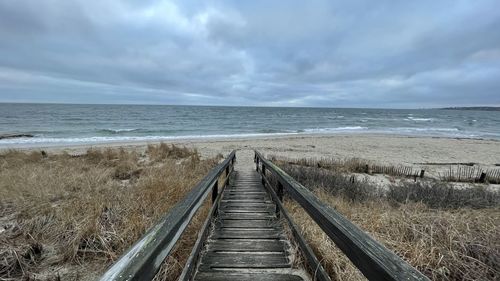 Boardwalk leading towards sea against sky
