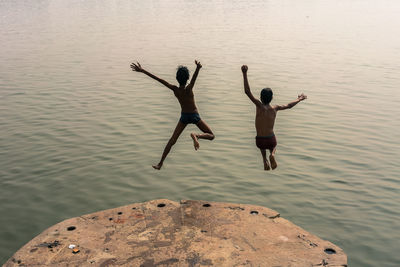 Full length of men jumping on rock in sea