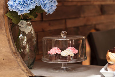 Close-up of cupcakes in cakestand by blue hydrangeas in vase on table