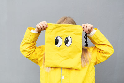 Girl holding yellow bag standing against gray background