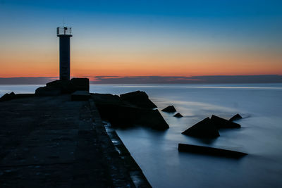 Lighthouse by sea against sky during sunset