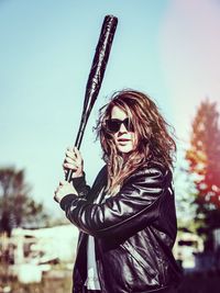 Woman holding baseball bat against sky on sunny day