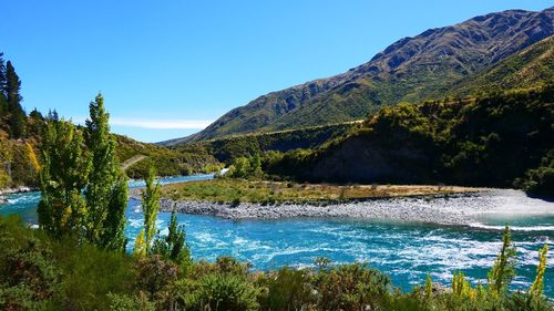 Scenic view of river by mountains against clear blue sky