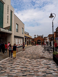 People walking on street amidst buildings in city against sky