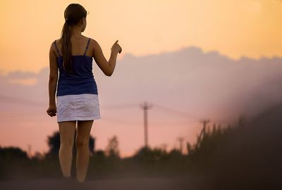 Rear view of woman walking on landscape against sunset sky