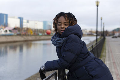 Young woman looking away while standing by canal