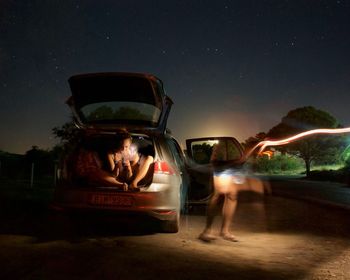 Man using smart phone against car at night