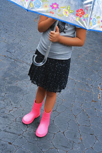 Low section of girl holding umbrella standing on footpath