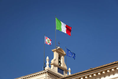 Low angle view of flags on bell tower against clear blue sky