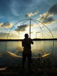 Rear view of man fishing in sea against sky