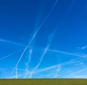 Scenic view of grassy field against sky with jet streams