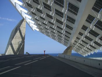 Low angle view of road below patterned built structure against sea