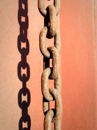 Close-up of rusty metallic chain against red wall