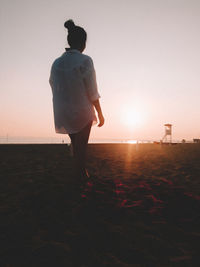 Rear view of woman standing on beach against sky during sunset