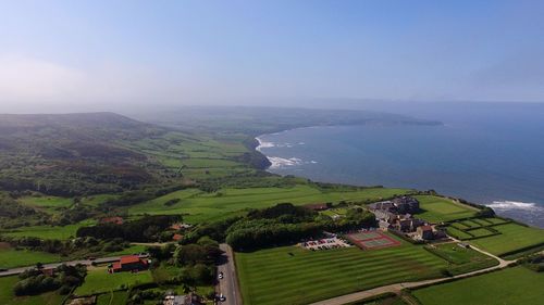 Aerial view of green landscape by sea against sky