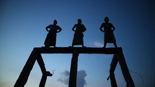 Low angle view of silhouette people standing against clear blue sky