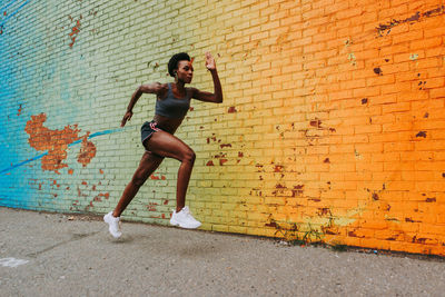 Woman running on road against brick wall in city