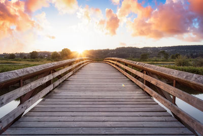 Wooden bridge against sky during sunset
