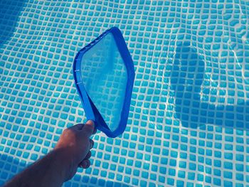 High angle view of hand holding mirror above swimming pool during sunny day