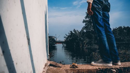 Low section of person by lake against sky