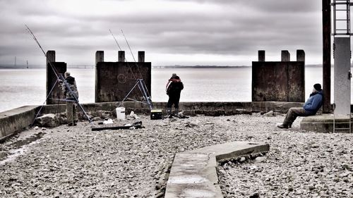 Woman sitting on bench by sea against cloudy sky