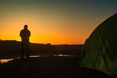 Rear view of man standing on mountain against sky during sunset