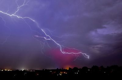 Lightning over illuminated cityscape against dramatic sky