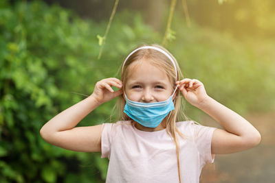 Happy little girl takes off protective medical mask from face outdoors. victory over coronavirus