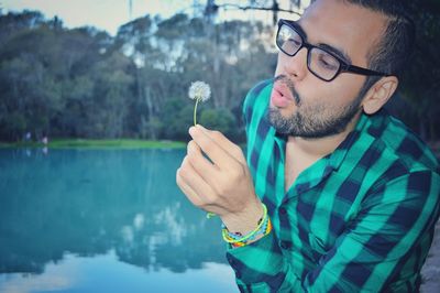 Young man blowing dandelion by lake