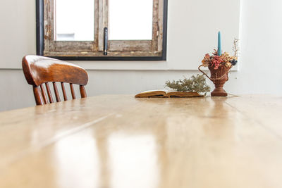 Open book by vase with candle on wooden table at home