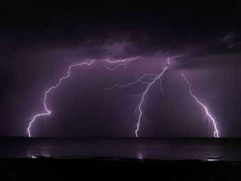 Firework display over sea against storm clouds