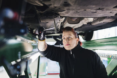 Female mechanic examining car with hammer in auto repair shop
