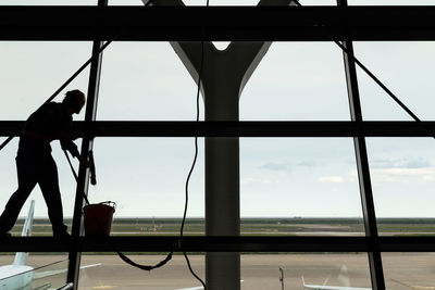 Silhouette people standing by window against sky