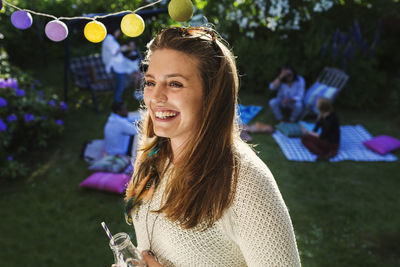 Happy young woman with friends in background at yard during summer party