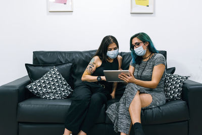 Two businesswomen wearing masks use a tablet in the office break