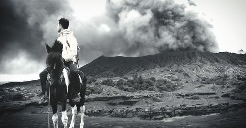 Man riding horse against volcanic mountain against sky