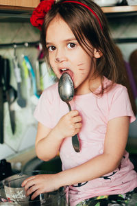 Cute toddler girl with face painting like a cat, licking spoon with honey sitting on table kitchen. 
