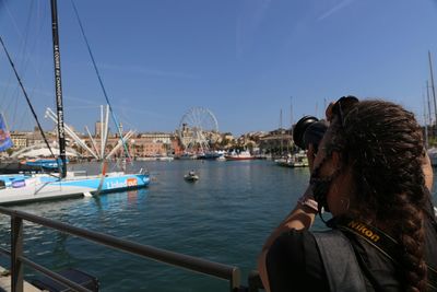 Rear view of woman photographing in city against sky