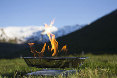 Burning flame outside portable grill, mountains and grass in the background. moment stopped.