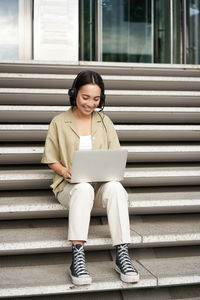 Young woman using mobile phone while sitting on staircase