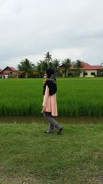 Side view of teenage girl walking at rice paddy against cloudy sky