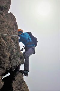 Low angle view of man rock climbing against clear sky