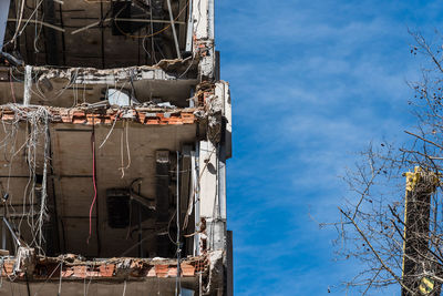 Bare trees by damaged building against sky