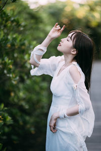 Side view of woman with arms raised standing against trees