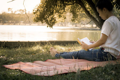 Side view of man reading book by lake at park