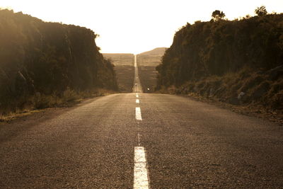 Country road amidst mountains on sunny day