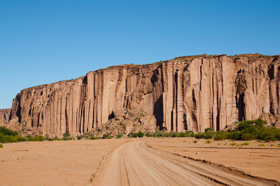 Road by rocky mountains against clear blue sky