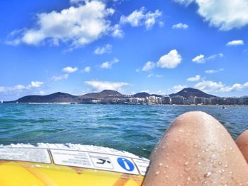 Low section of person relaxing on sea shore against sky