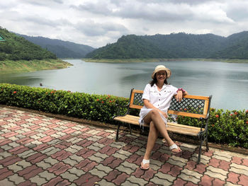 Full length portrait of woman sitting on bench against river