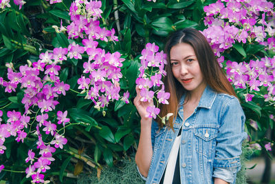 Portrait of beautiful young woman standing by purple flowering plants